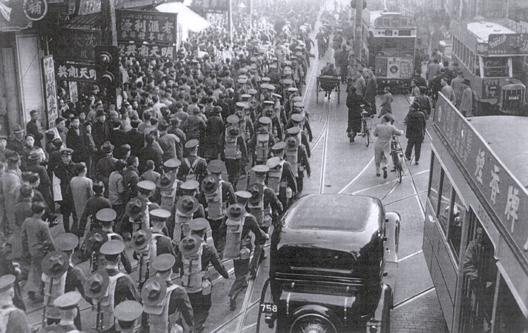 Troops of the First Battalion, Fourth Marines march down Nanking Road, on their way to the quays of the Whangpoo River preparatory to embarking on U.S. President Line ships for the Philippine Islands. The Marines share the crowded streets with examples of every mode of transportation available.